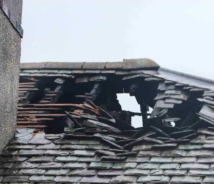 Fire damage to a roof leaves a hole and charred shingles.